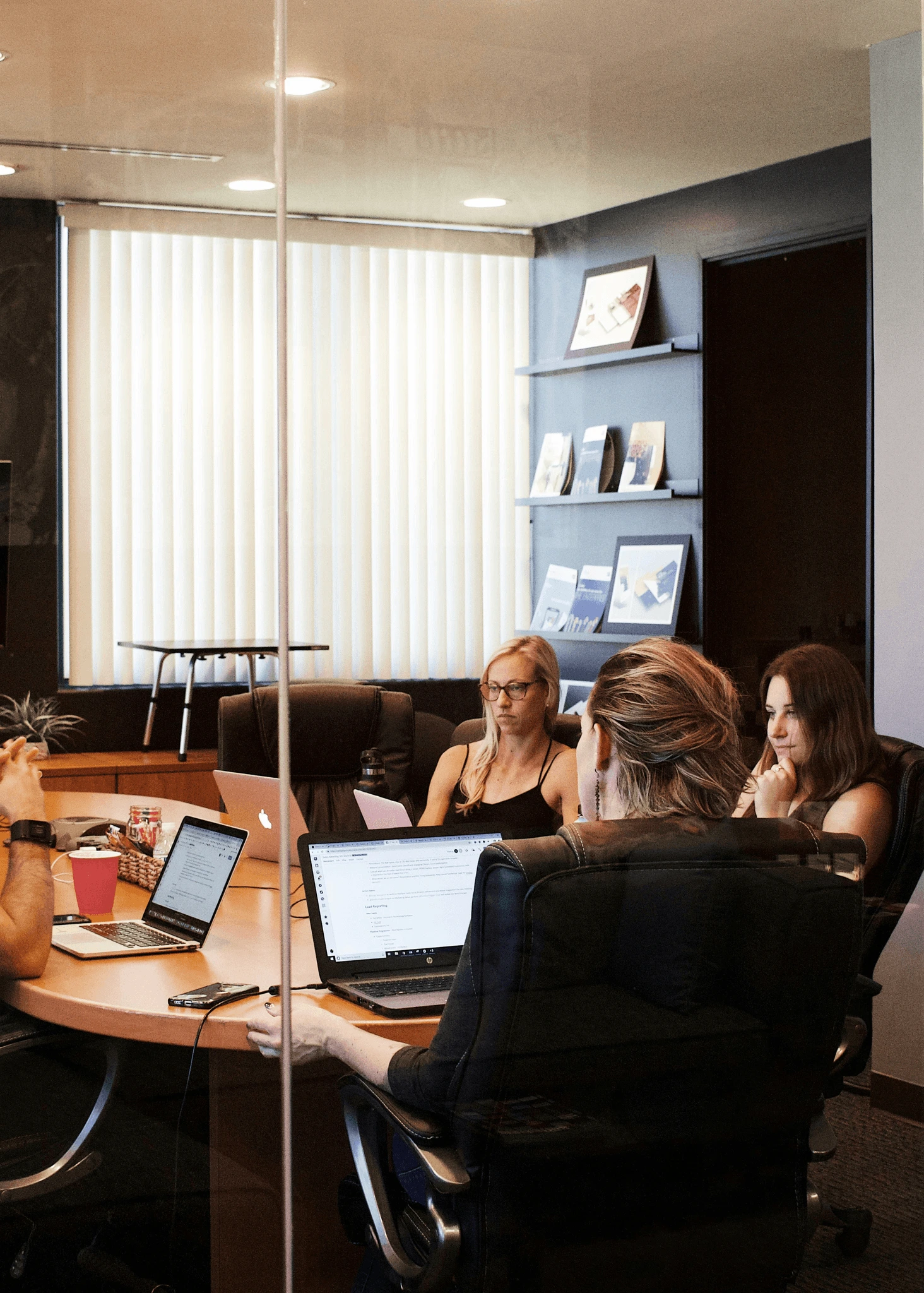 Three people sit with laptops in a glass-walled law firm meeting room discussing case files – Blursafe pseudonymizes case files before they are shared.