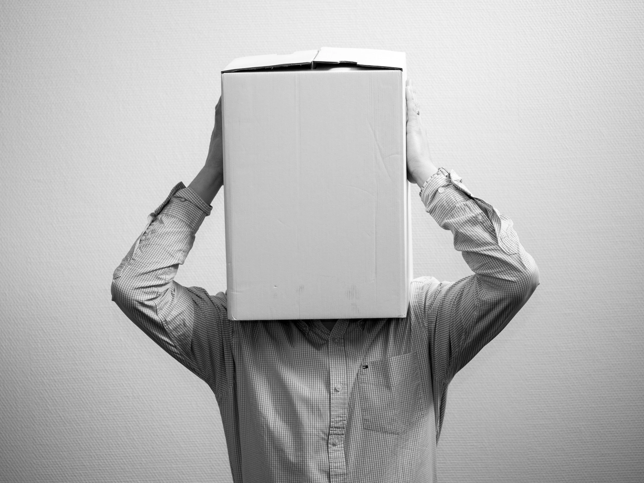 Mann in weißem Hemd hält sich einen Karton über den Kopf – Sinnbild für unvollständige Anonymisierung, bei der sensible Daten weiterhin erkennbar bleiben.